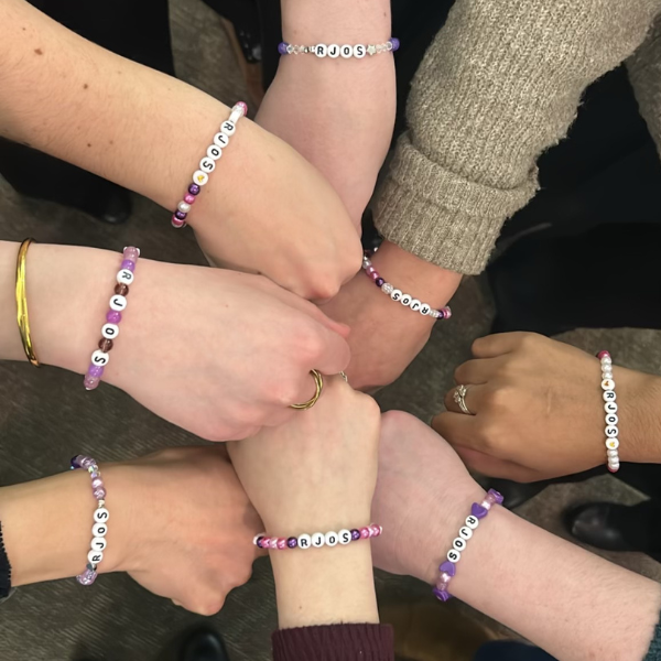 A group of hands linked together all wearing event specific braclets.